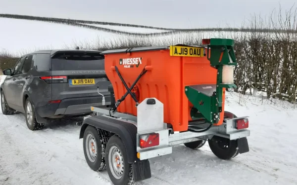 Wessex Polar One Salt And Grit Spreaders | Middlewich Machinery A wessex polar one salt and grit spreader, painted in orange, is parked on the roadside with a vast, snowy landscape in the background.
